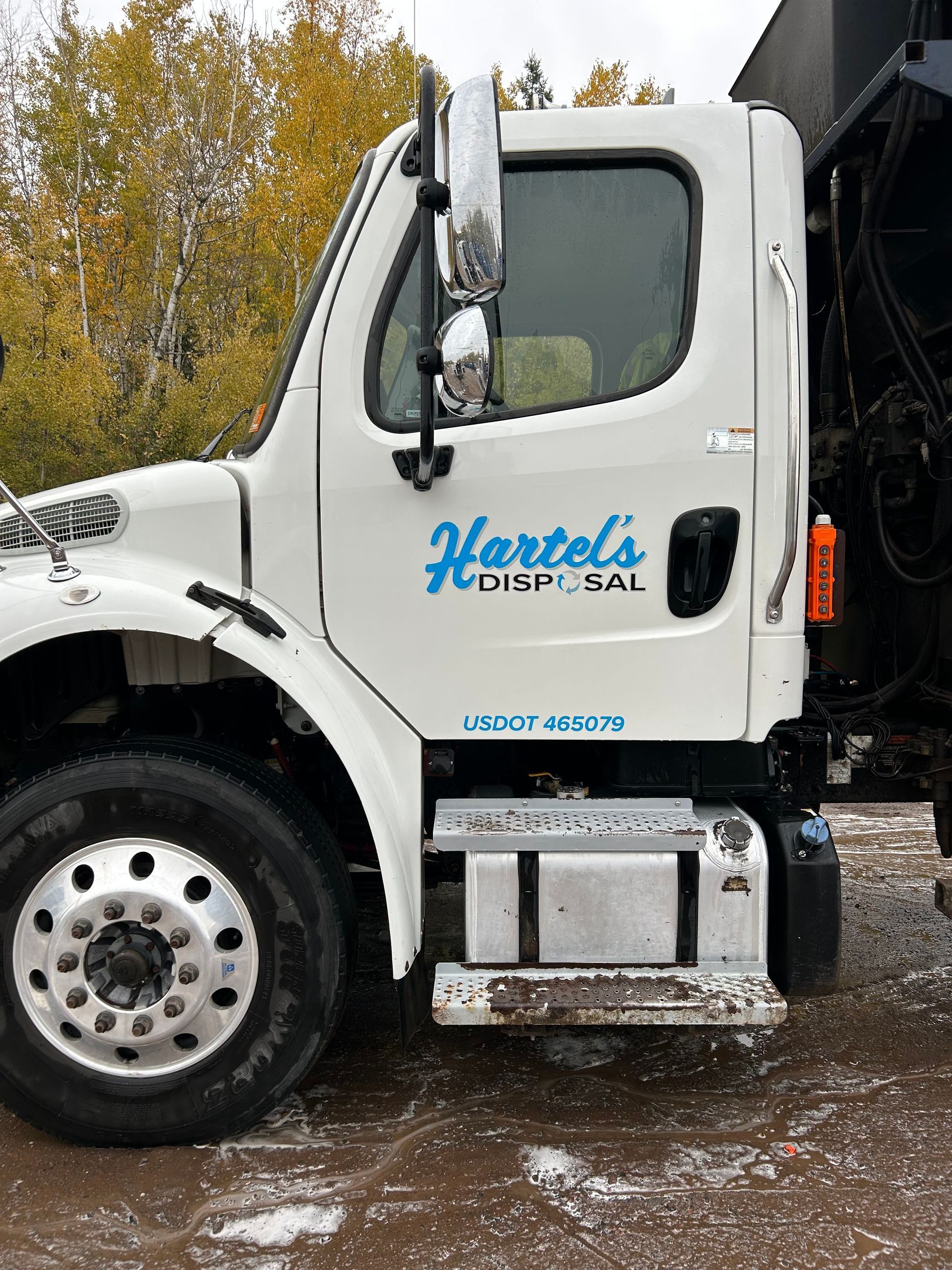An after image of a clean white garbage truck is parked in a dirt lot