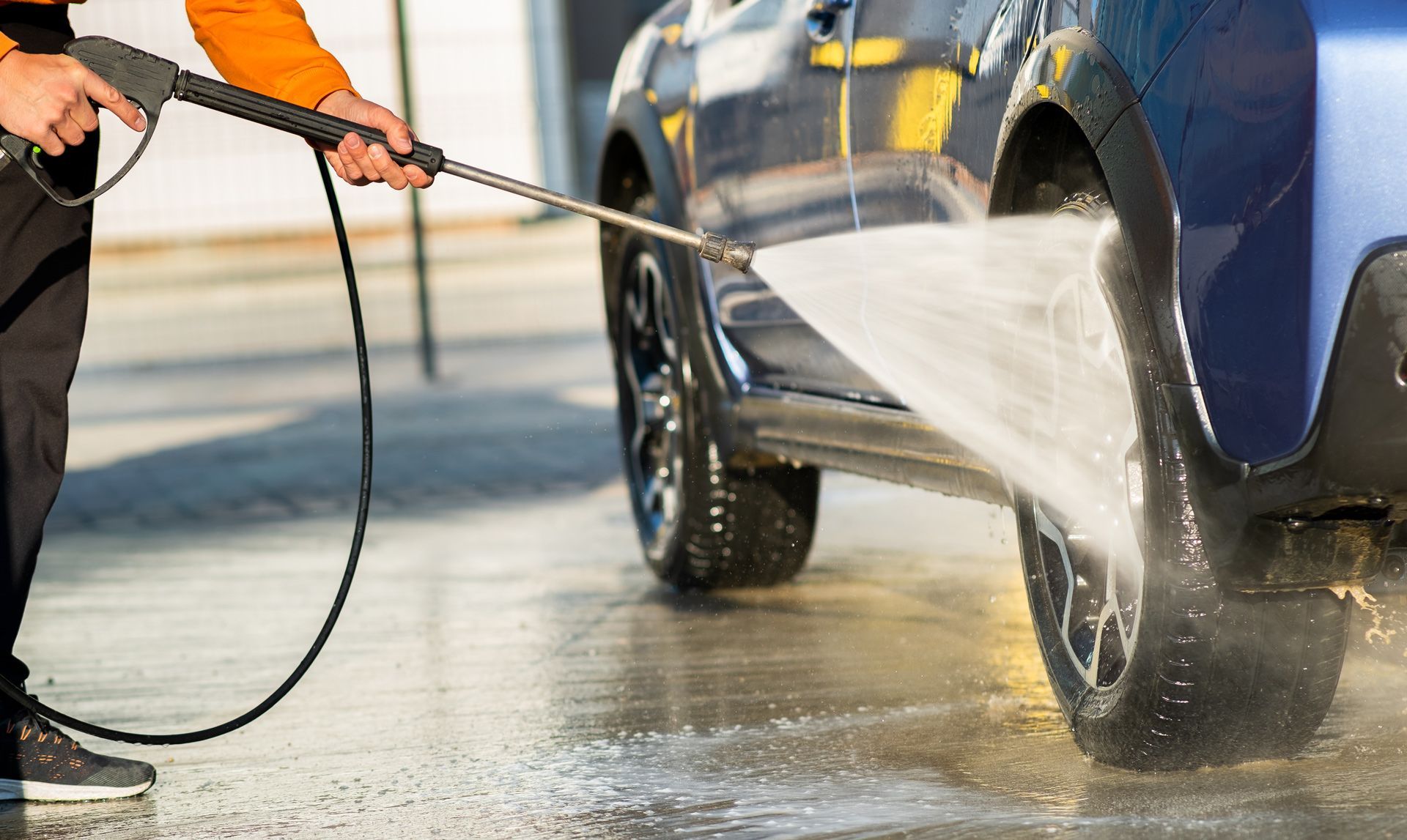 Person washing a blue car with a pressure washer.