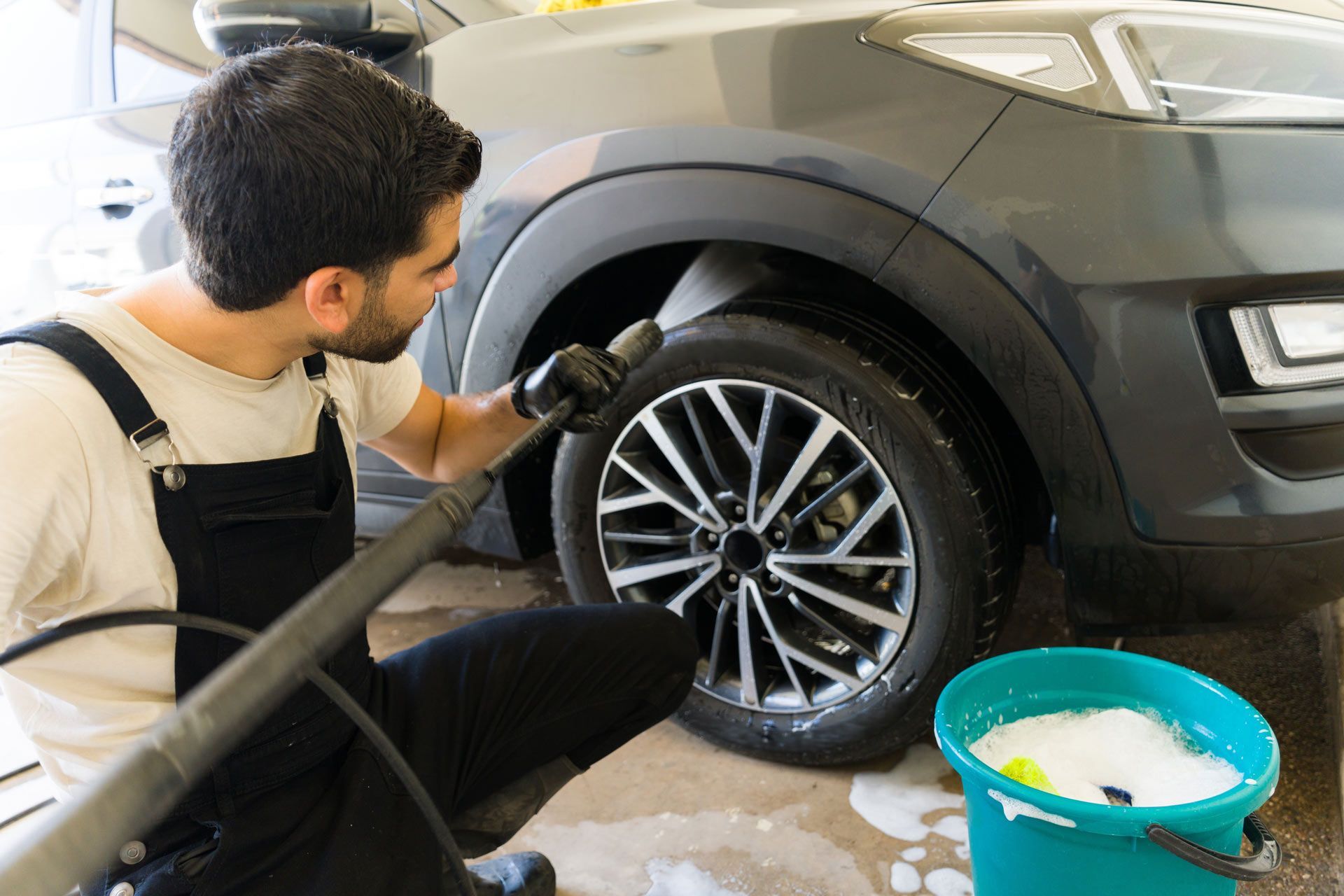 A man is cleaning a car wheel with a high pressure washer