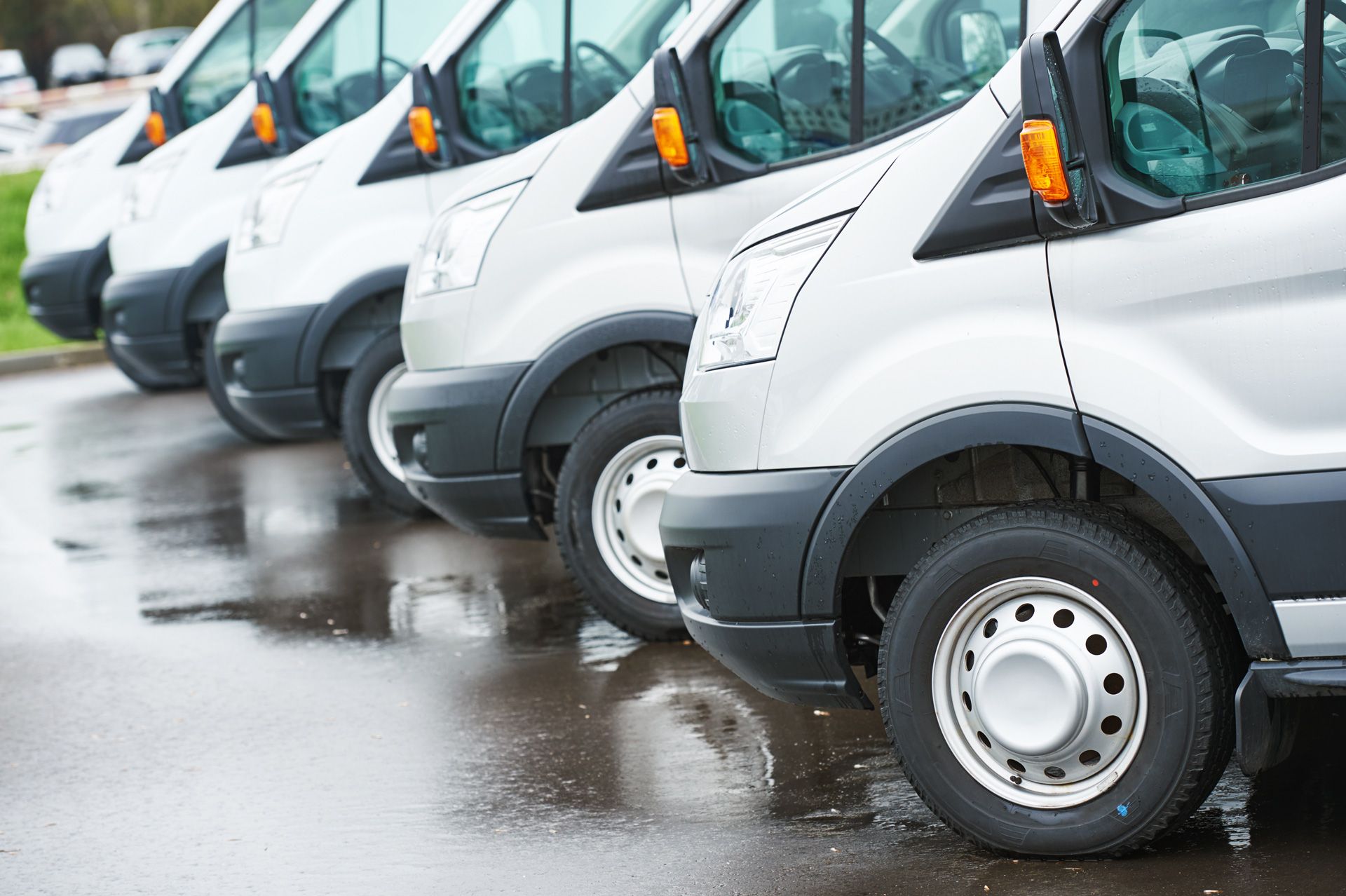 Row of white cargo vans parked on wet pavement.