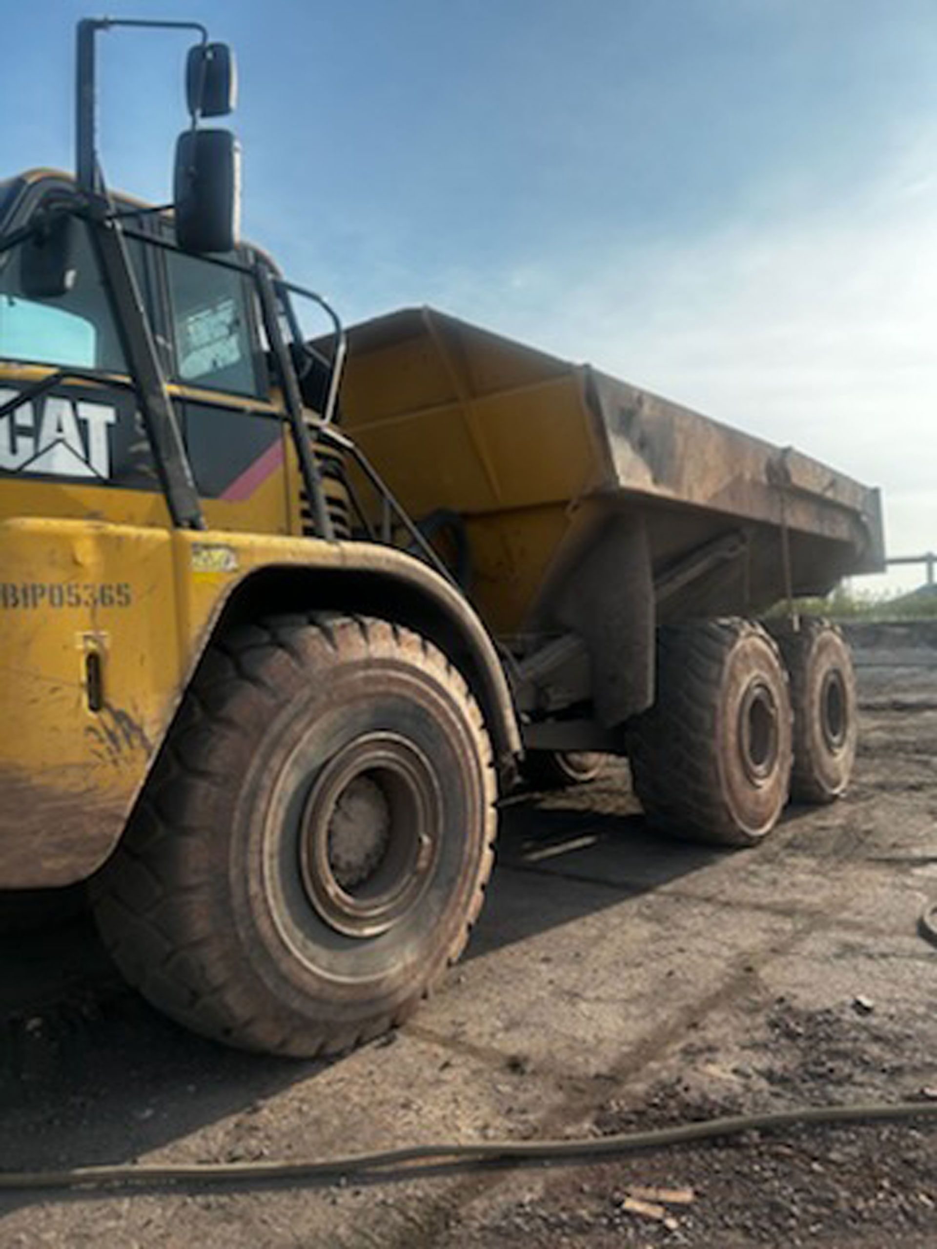 A yellow cat dump truck is parked in a dirt lot