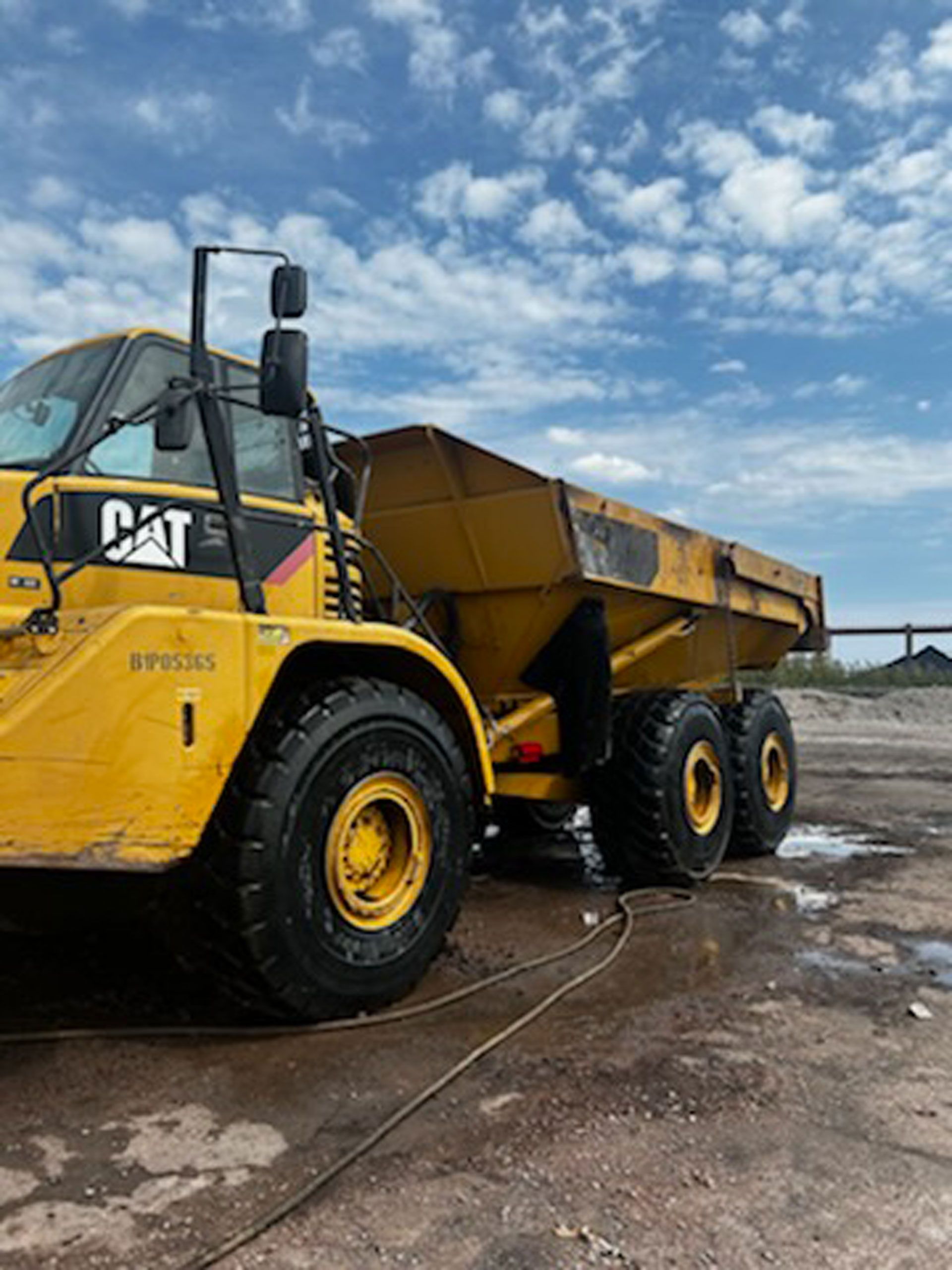 A yellow cat dump truck is parked in a dirt field