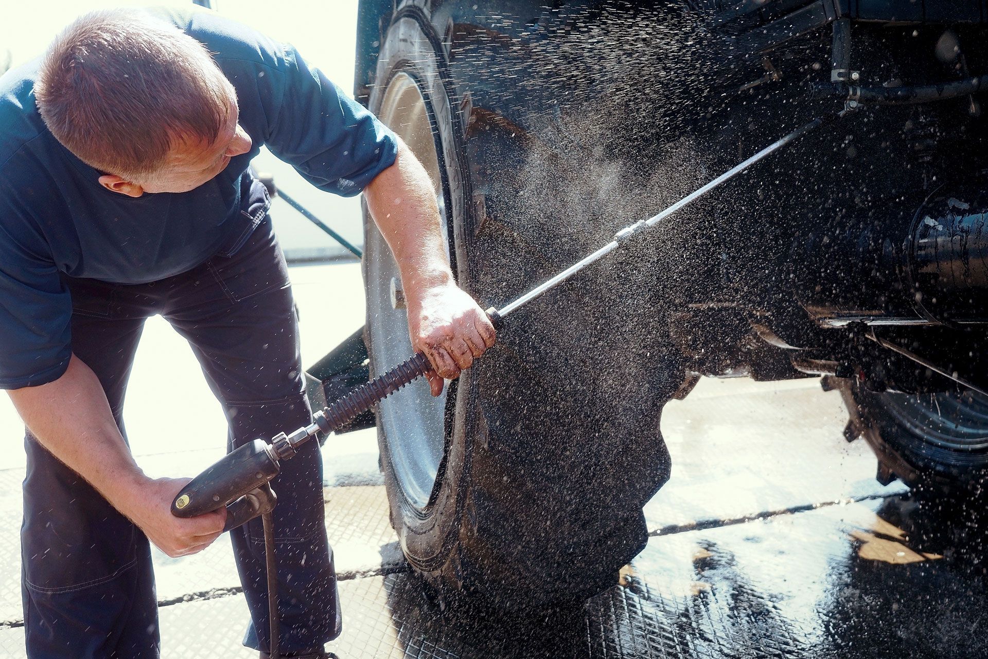 Man power washing a tractor tire, water spraying, outdoors.