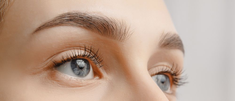 Close-up of a person's eyes, looking up and to the side, with thick, filled-in eyebrows and long eyelashes.