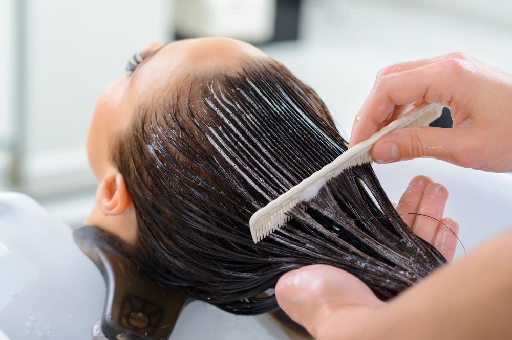 Person having hair treated with product at a salon; comb being used on wet hair.