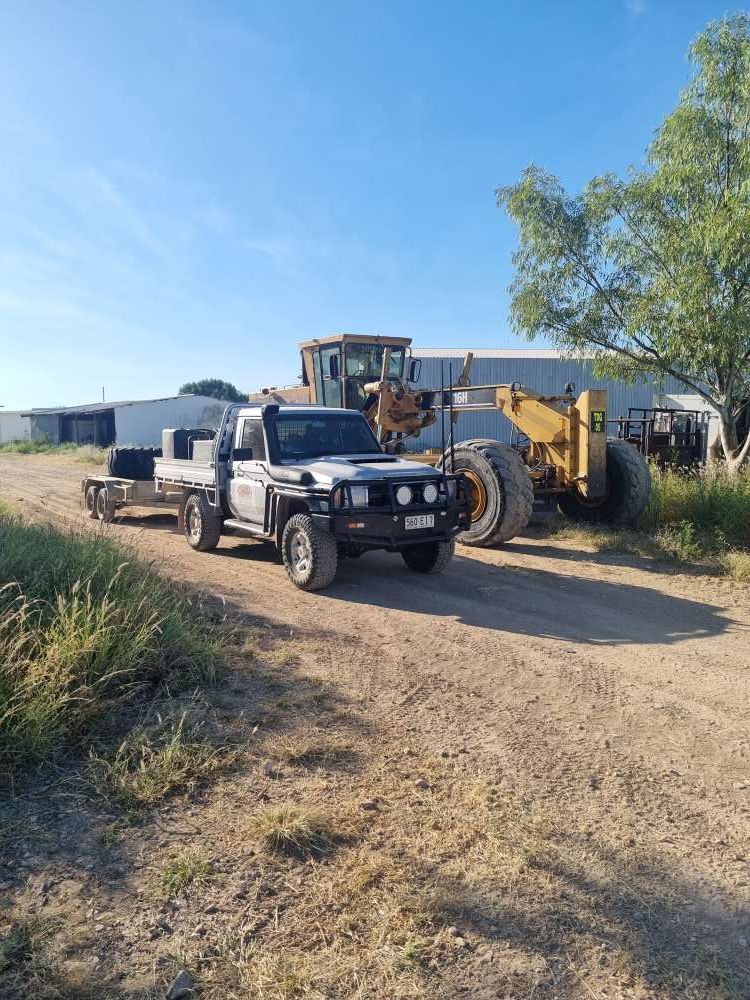 A Truck is Towing a Bulldozer Down a Dirt Road — Burnett Contracting in Cloncurry, QLD