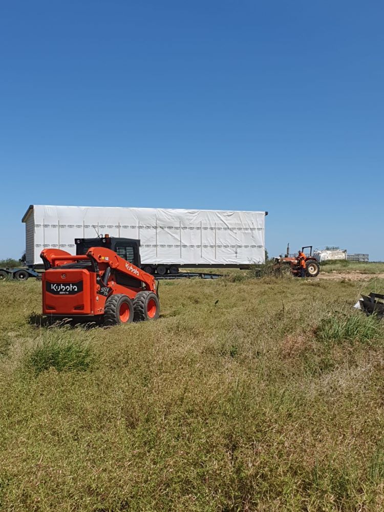 Small Orange Tractor is Driving Through a Grassy Field — Burnett Contracting in Cloncurry, QLD