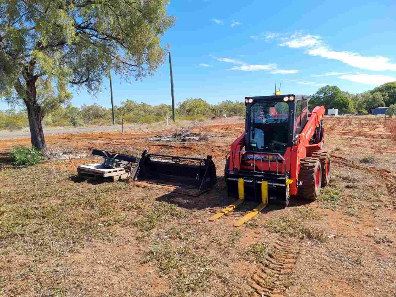 Red Tractor is Driving Through a Dirt Field Next to a Tree — Burnett Contracting in Cloncurry, QLD