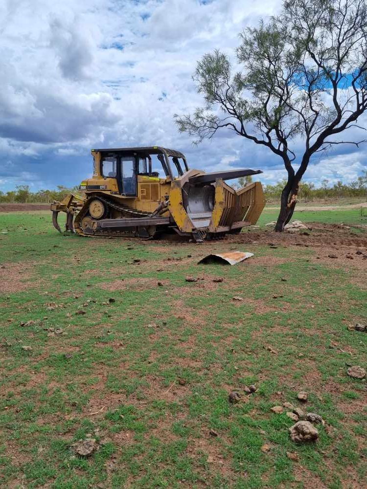 Bulldozer is Parked in a Grassy Field Next to a Tree — Burnett Contracting in Cloncurry, QLD