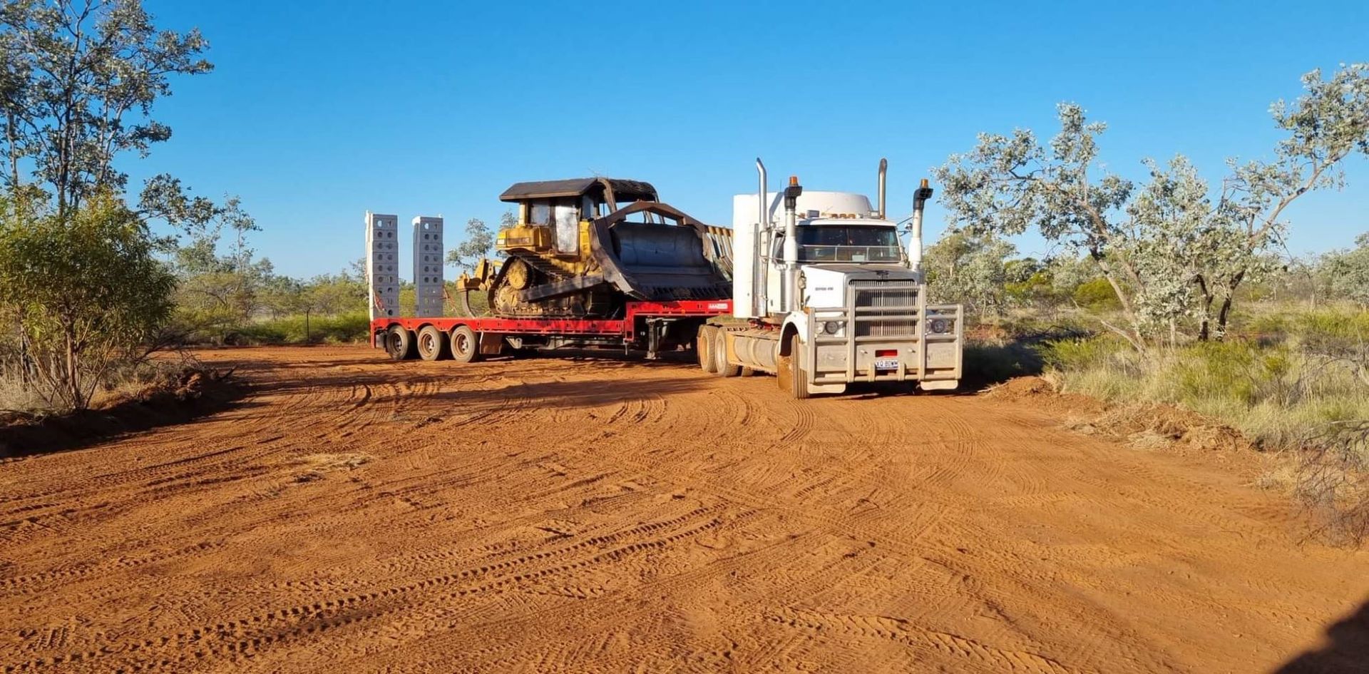 Semi-Truck Hauling a Bulldozer on a Red Dirt Road — Burnett Contracting in Cloncurry, QLD