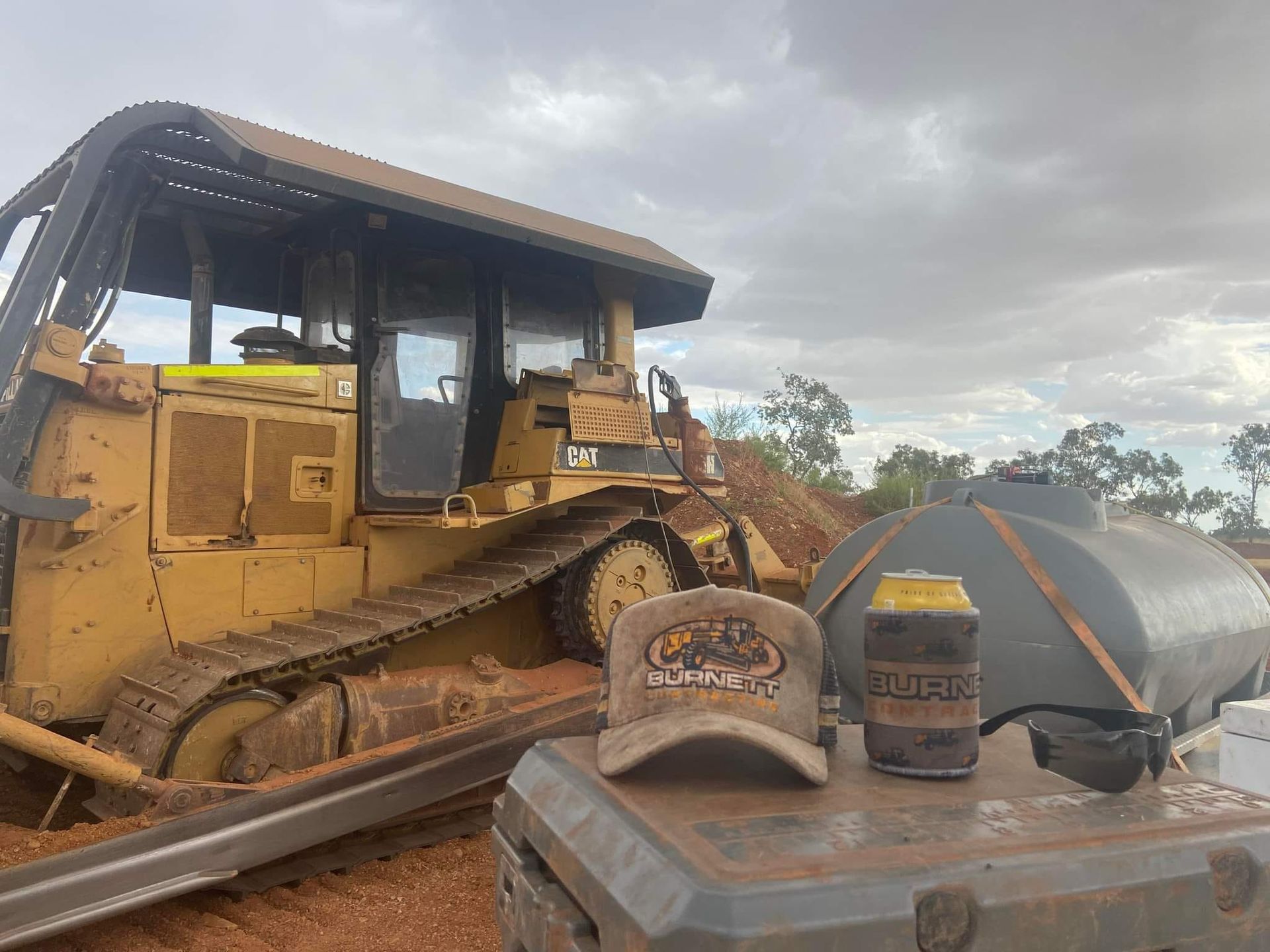 Yellow Bulldozer With a Cap and Drink on a Muddy Surface in an Outdoor Setting — Burnett Contracting in Cloncurry, QLD