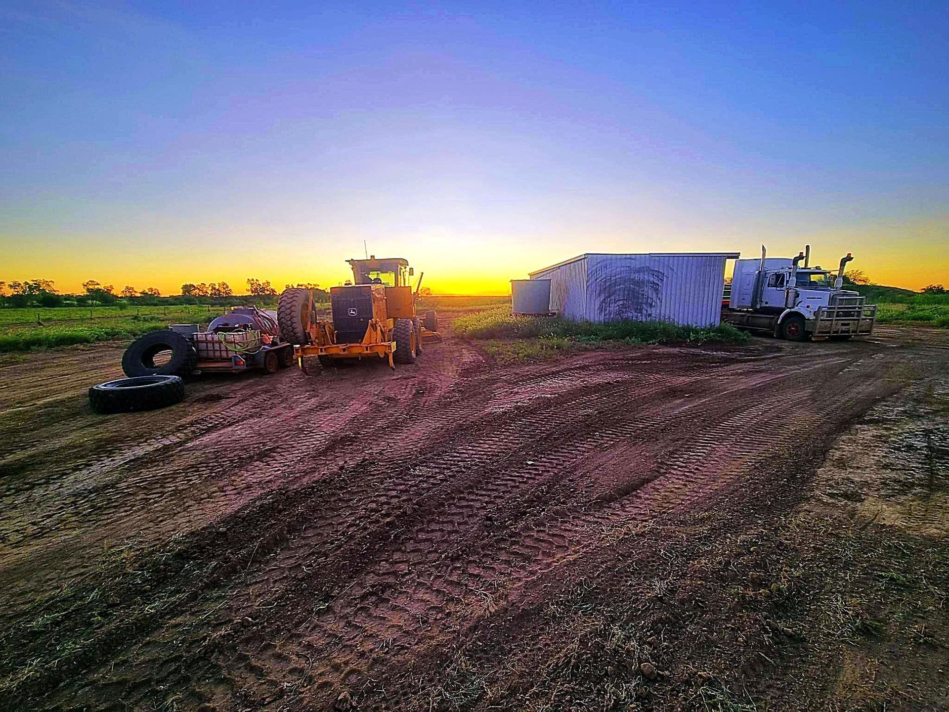 A Sunrise Illuminates Heavy Machinery Including a Grader, Truck, and Tires — Burnett Contracting in Cloncurry, QLD