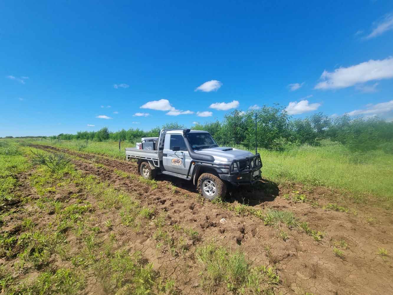 A White Truck is Driving Down a Dirt Road in a Field — Burnett Contracting in Cloncurry, QLD