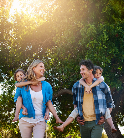 Family walking outdoors, parents carrying children piggyback style, sunny day.
