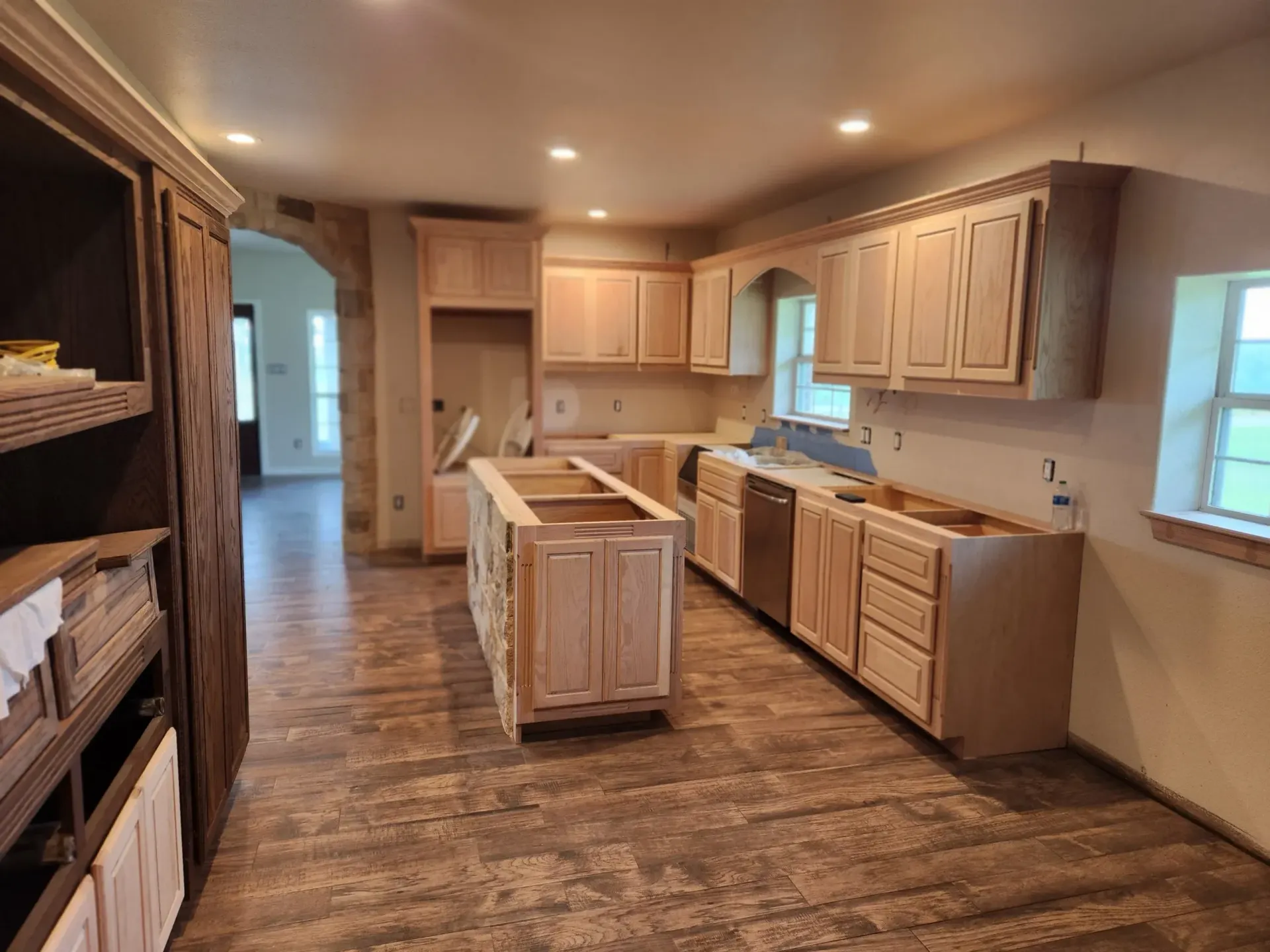 Kitchen under renovation with light wood cabinets, an island, and exposed subfloor.
