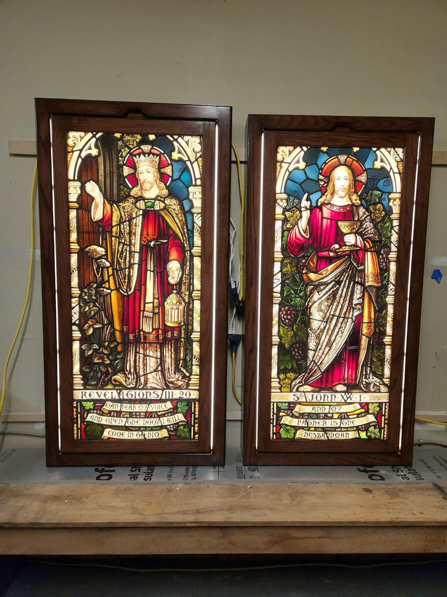 Two backlit stained glass panels with figures in frames; brown frames.