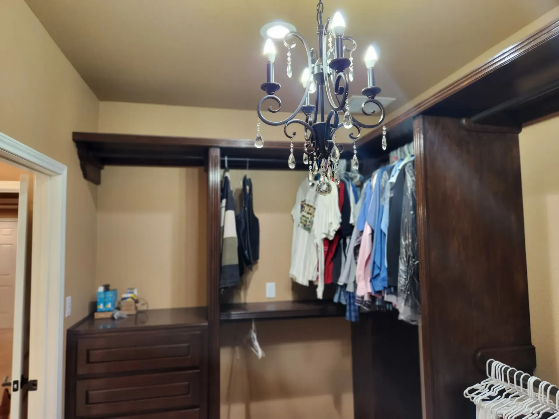 Walk-in closet with dark wood shelving and a chandelier, clothes hanging on racks.