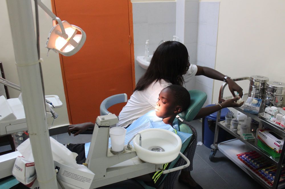 A young boy is sitting in a dental chair with a woman behind him.