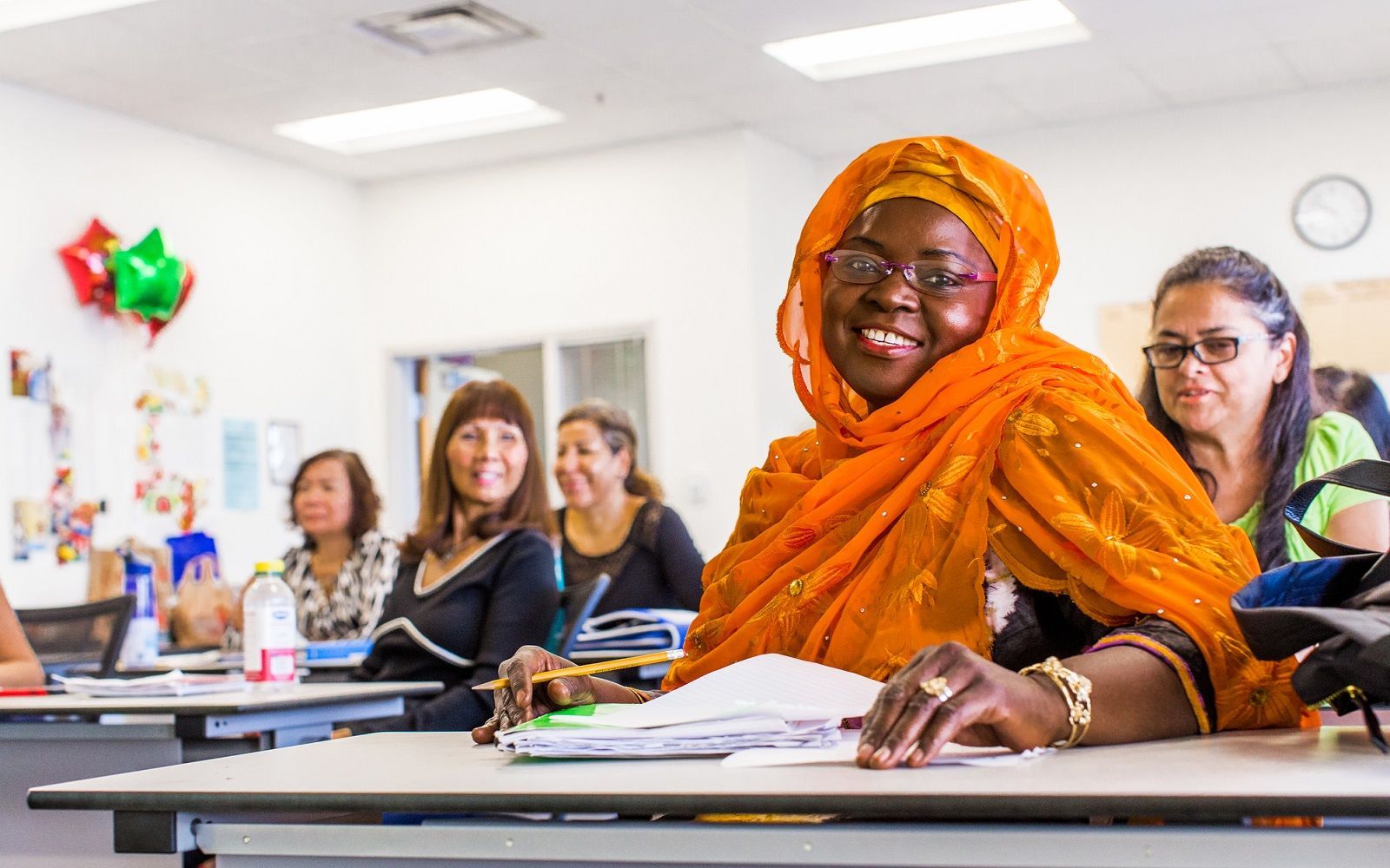 A woman in an orange scarf is sitting at a desk in a classroom.