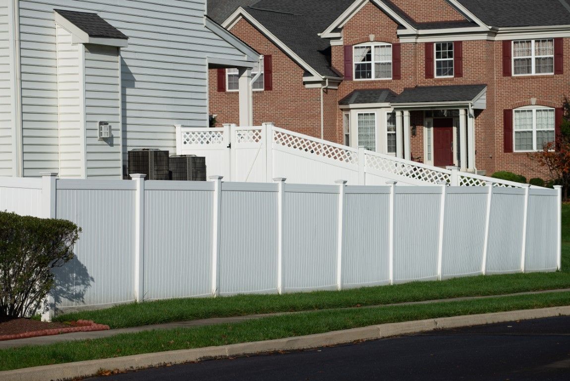 A suburban scene with two houses, one gray and one brick, separated by a white vinyl fence.