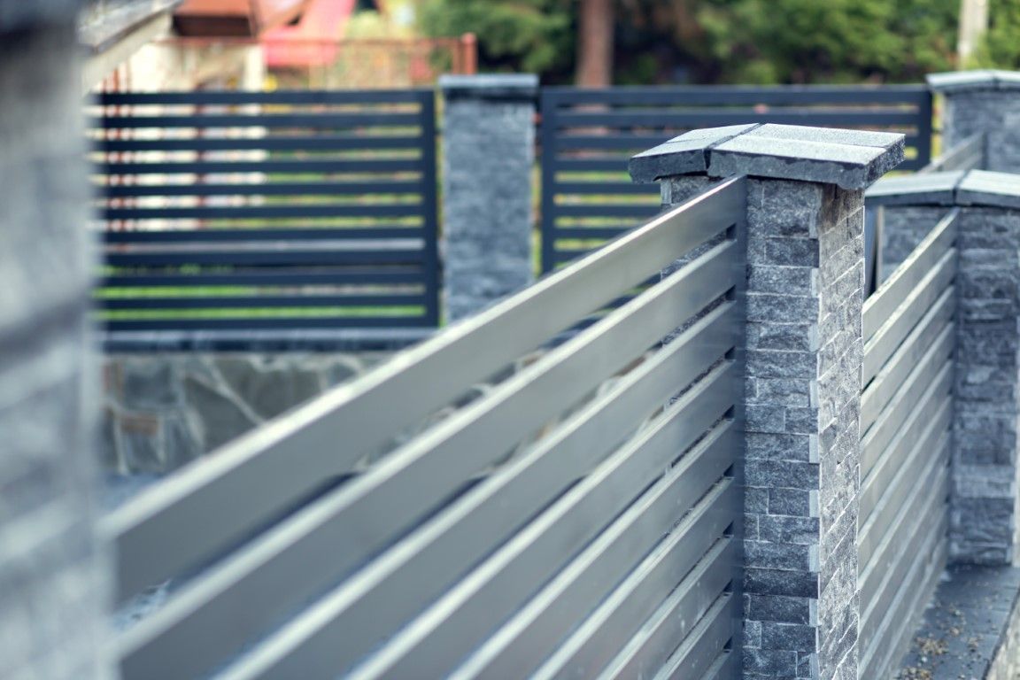 Modern gray fence with horizontal metal slats and stone pillars, creating a sleek and structured appearance. 
