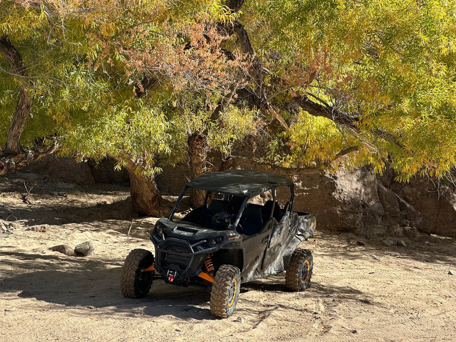 An all-terrain vehicle parked in a sandy area under vibrant yellow-leaved trees, surrounded by rocky terrain.