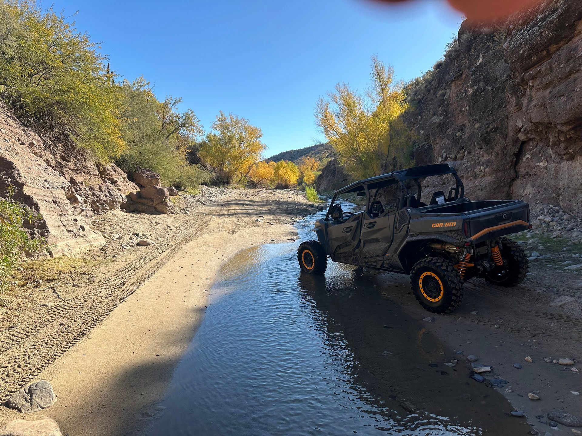 A black atv is driving down a dirt road next to a river.