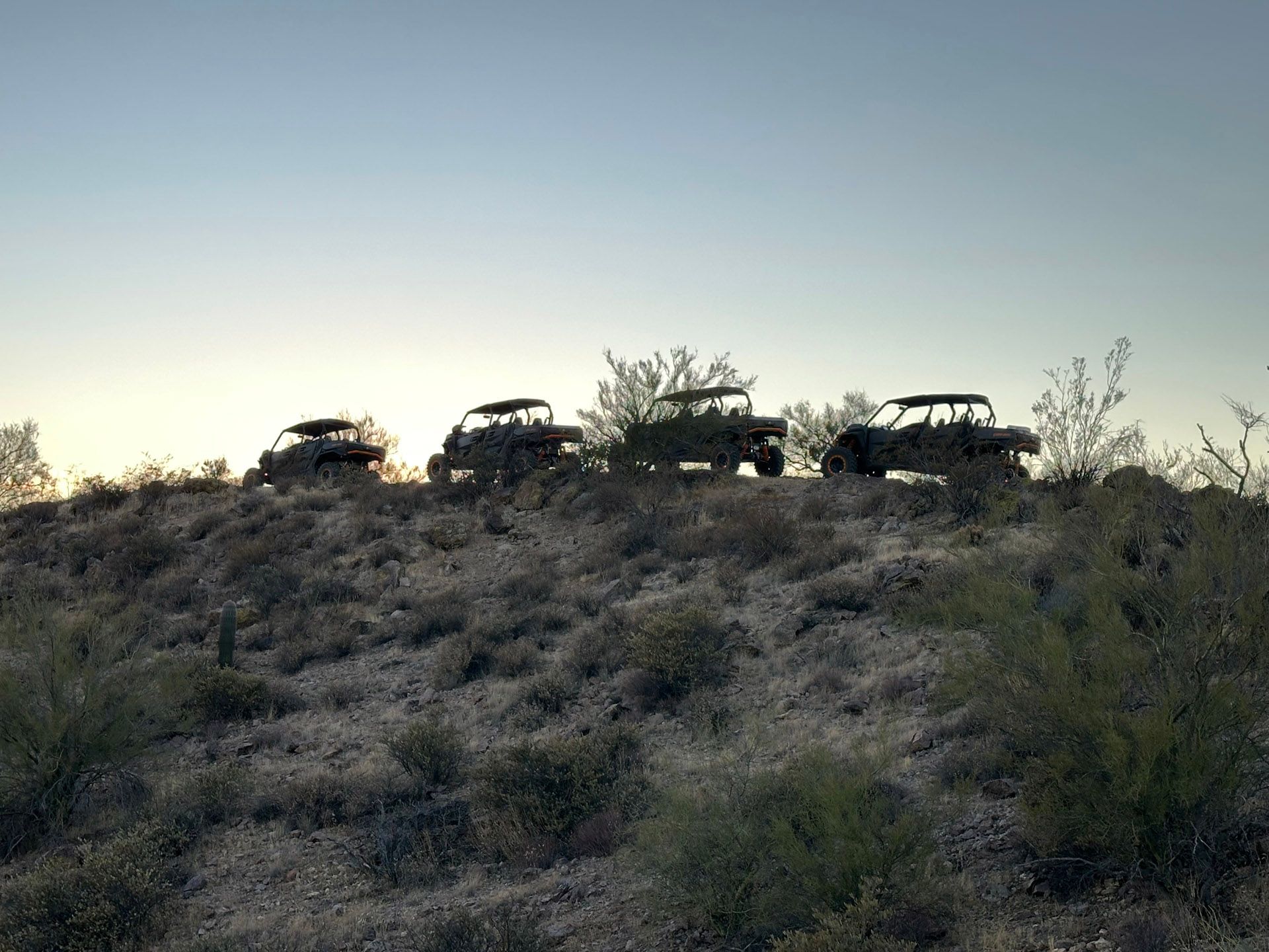 Three atvs are parked on top of a hill in the desert.
