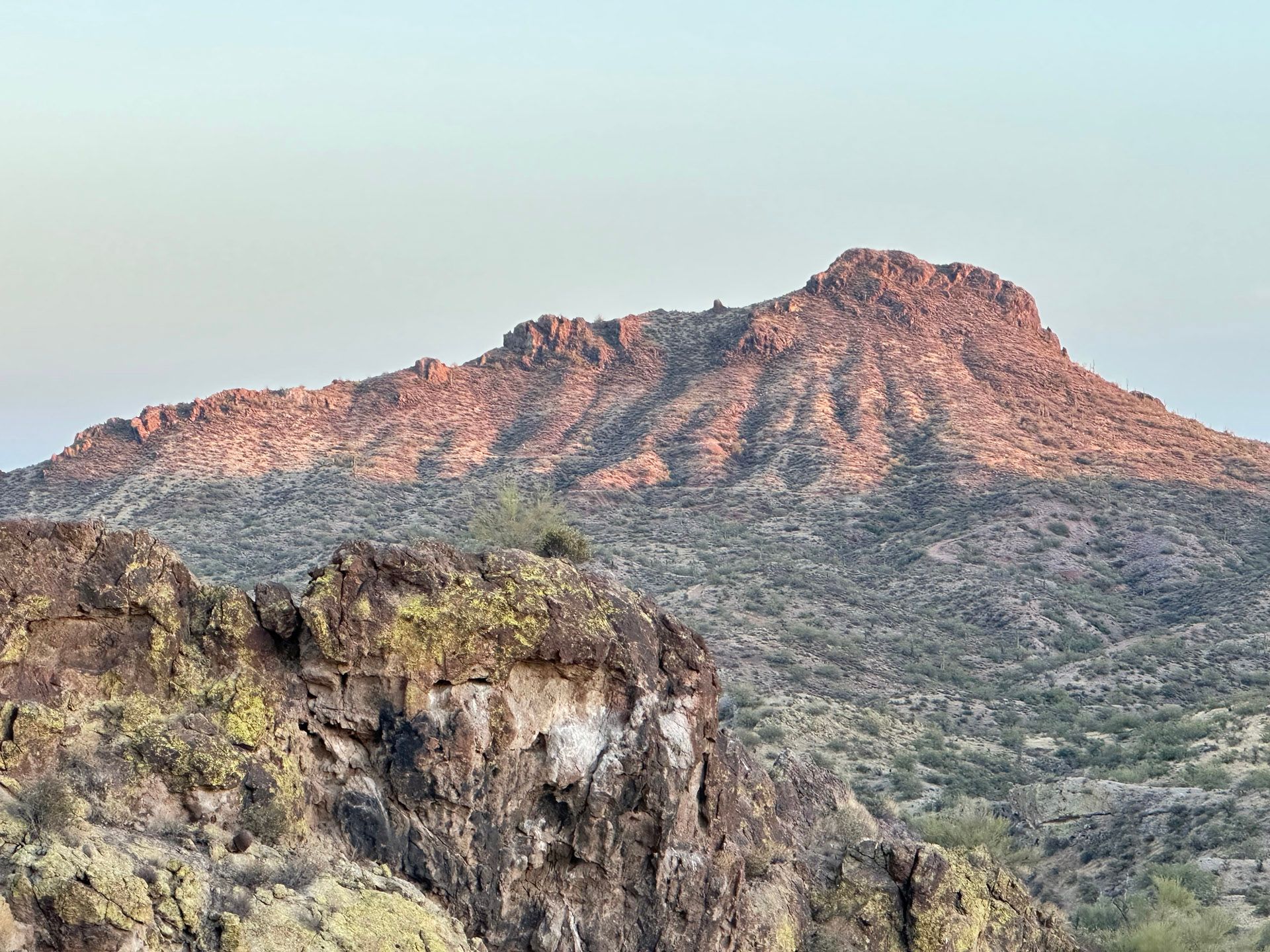 A mountain in the middle of a desert with a blue sky in the background.