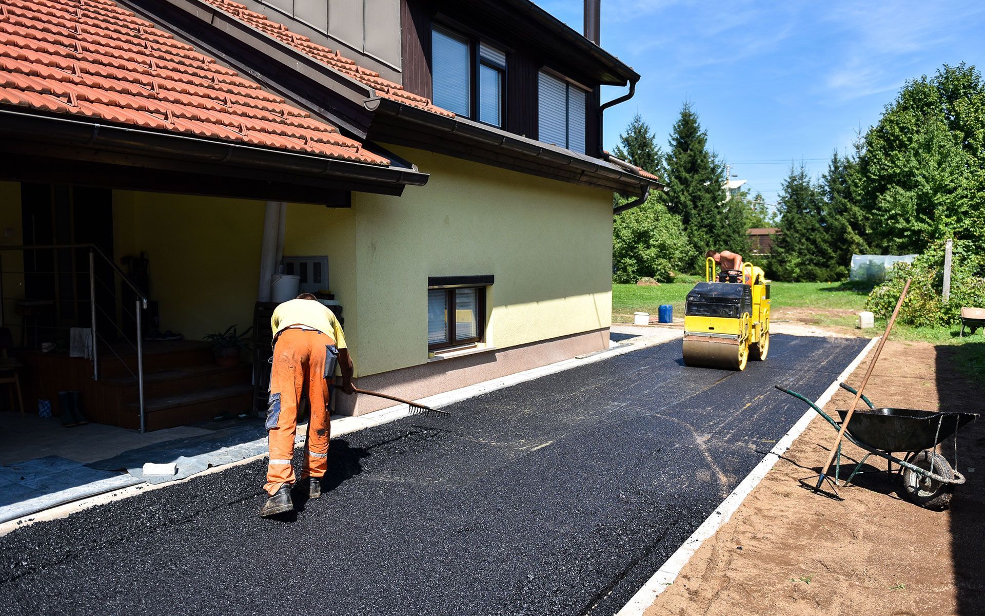 A man is laying asphalt on a driveway in front of a house.