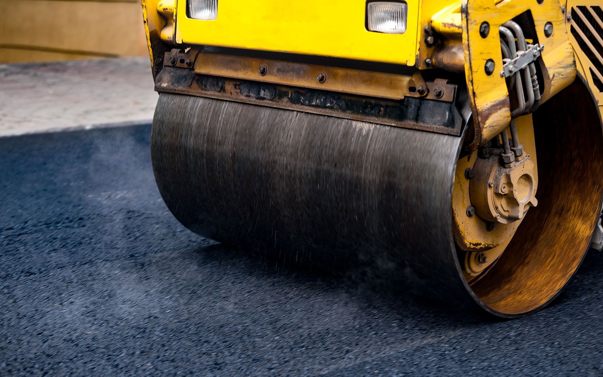 A yellow roller is rolling asphalt on a road.