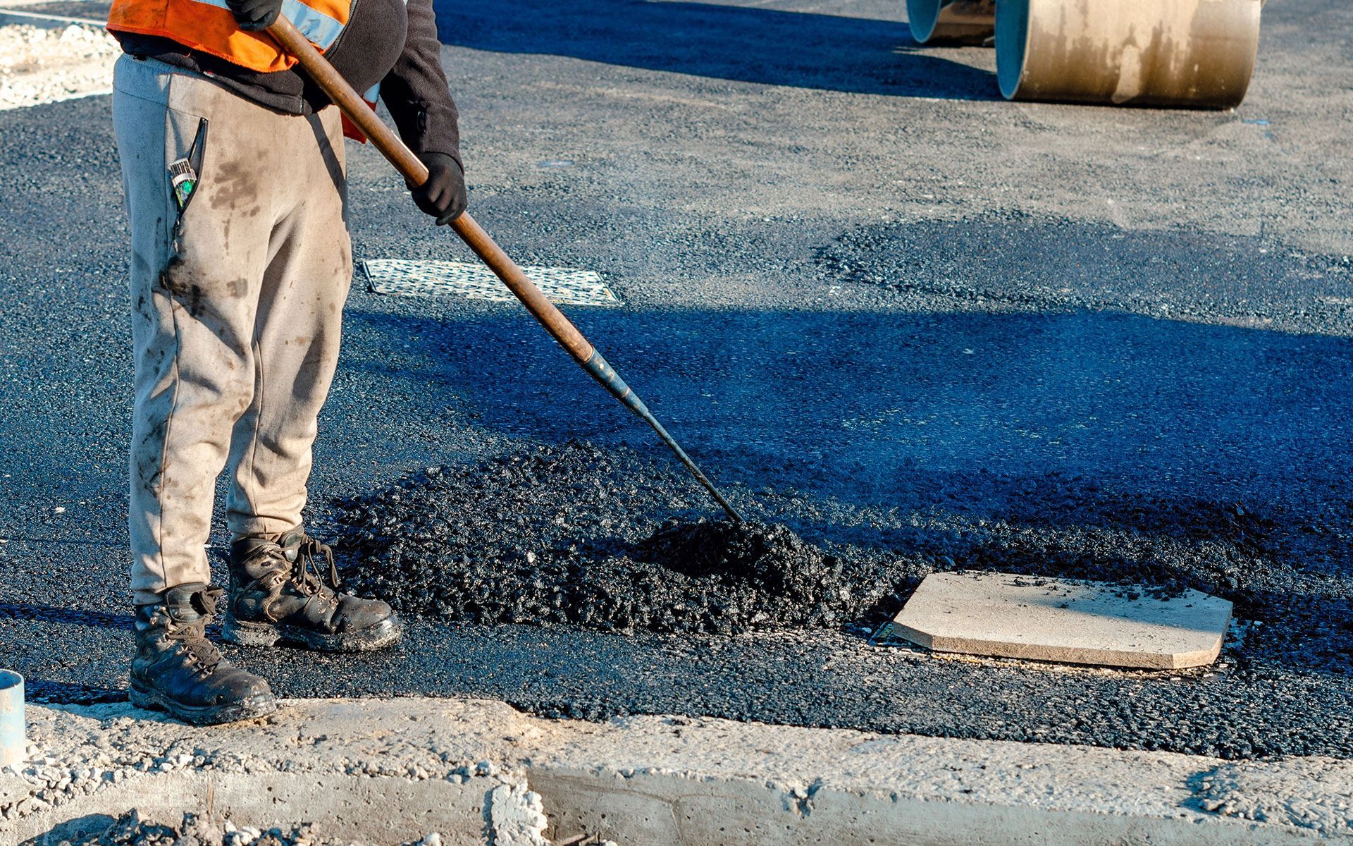 A man is spreading asphalt on a road with a shovel.