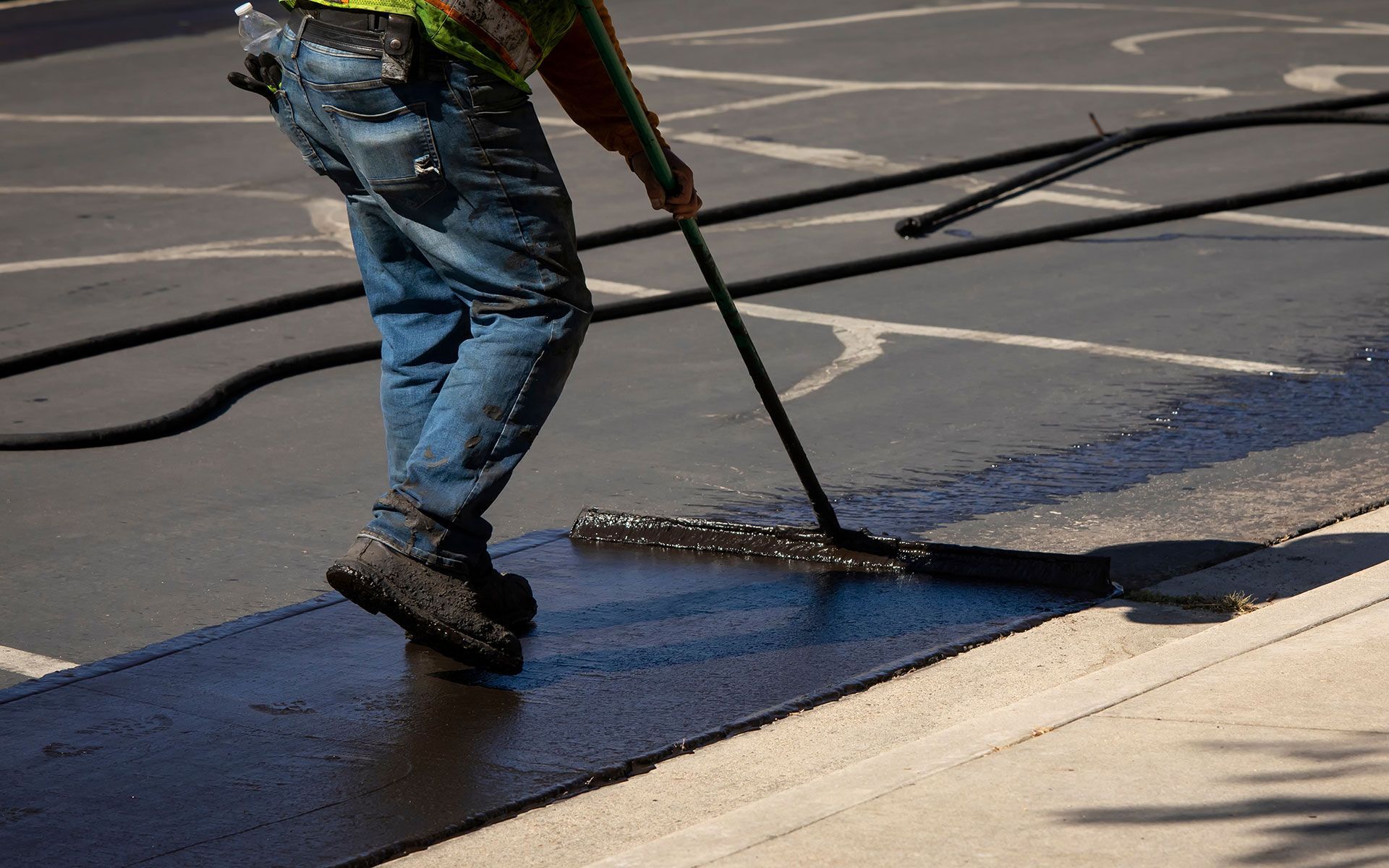 A man is painting a parking lot with a broom.