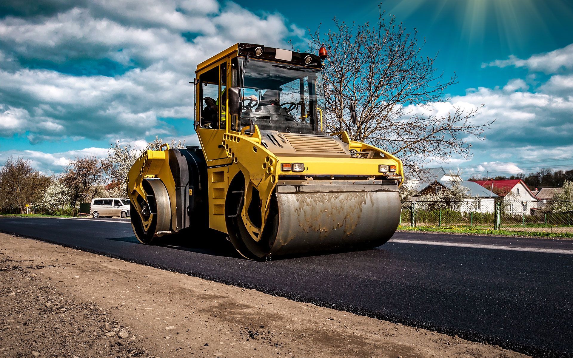 A yellow road roller is driving down a road.