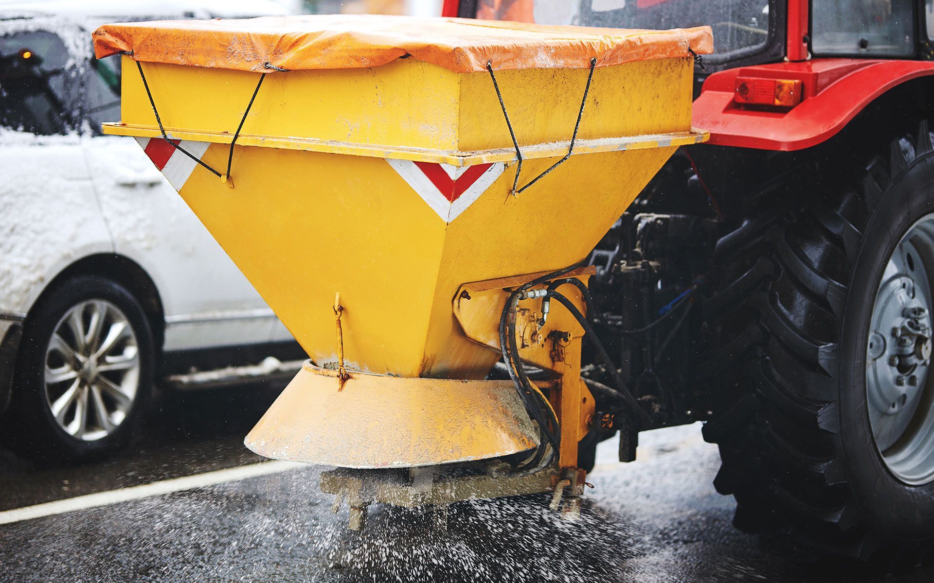 A tractor is spreading salt on the road next to a car.