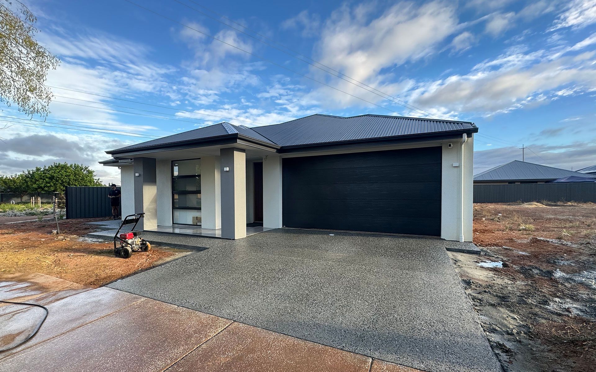 A house with a black garage door is sitting on top of a dirt field.