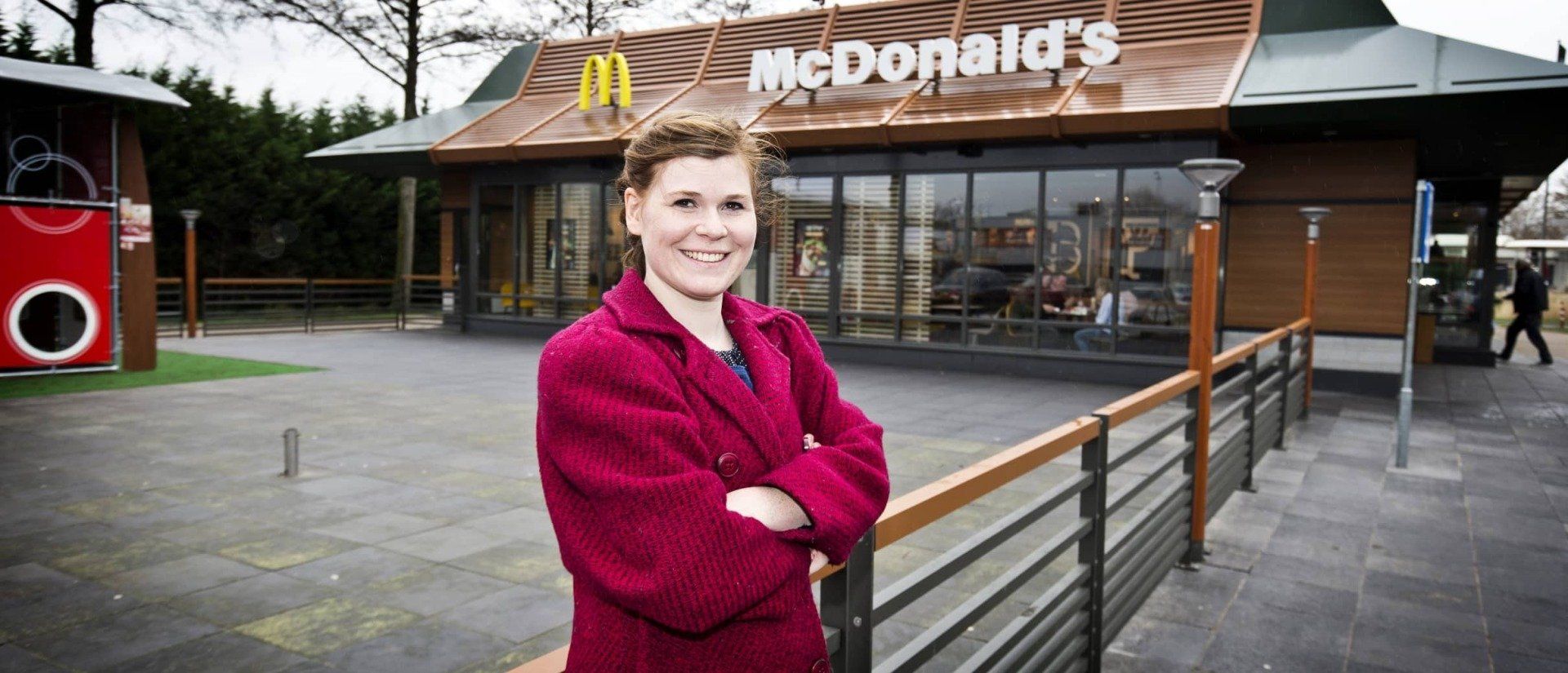 Een vrouw in een rode jas staat voor een McDonald's restaurant.
