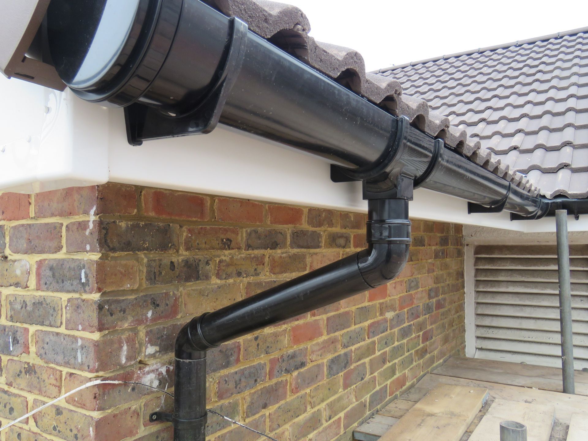 A black gutter is attached to the side of a brick building.