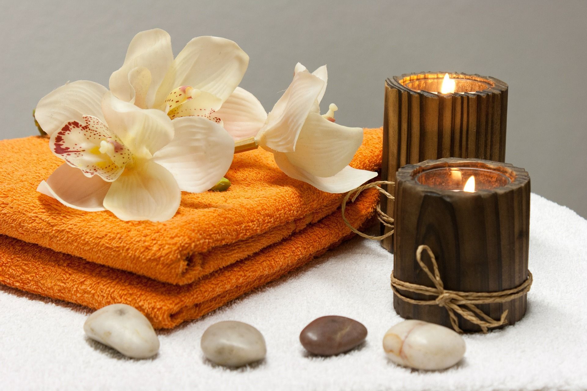 A stack of towels, candles, rocks and flowers on a table.