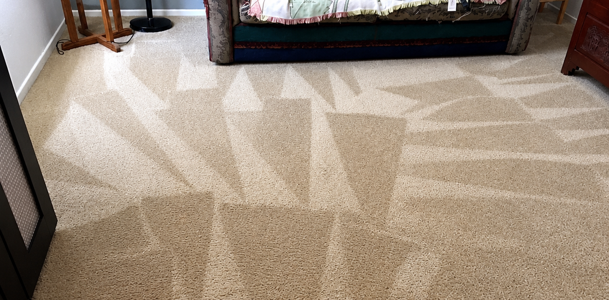 Beige carpet with light patterns in a living room, with a sofa edge at the top
