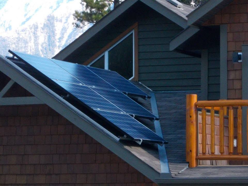 Solar panels mounted on a sloped roof beside a wooden deck railing.
