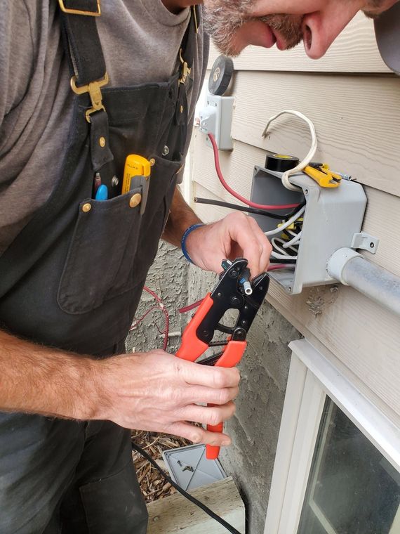 Technician using a red tool to work on outdoor electrical wiring beside a house