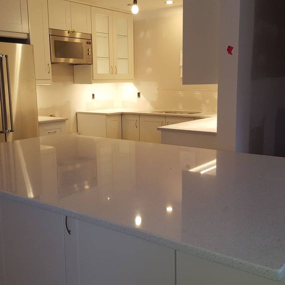 Bright modern kitchen with white cabinets, stainless steel appliances, and glossy white countertops