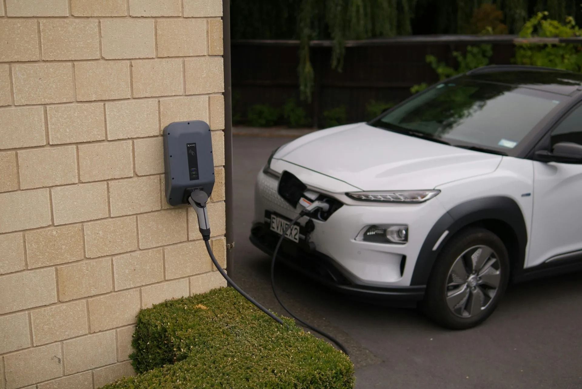 Damaged white SUV charging at a wall-mounted EV station beside a brick building