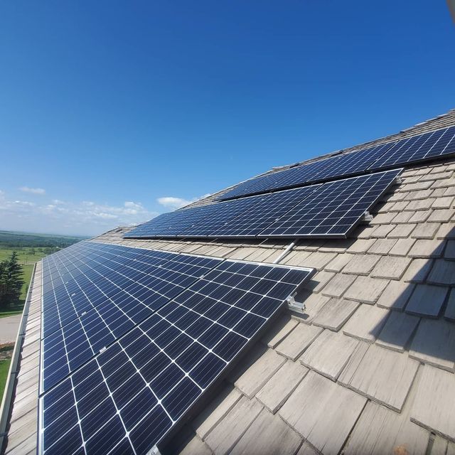 Solar panels installed on a sloped shingle roof under a clear blue sky