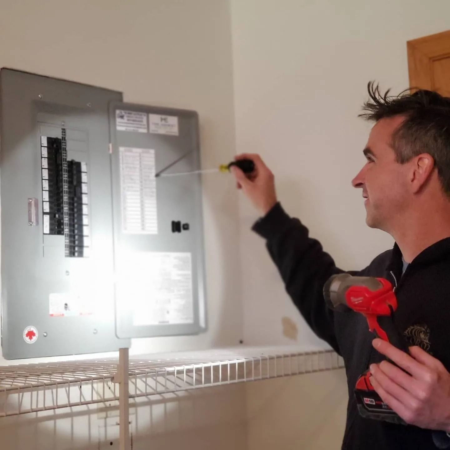 Man pointing with a screwdriver at an electrical breaker panel indoors