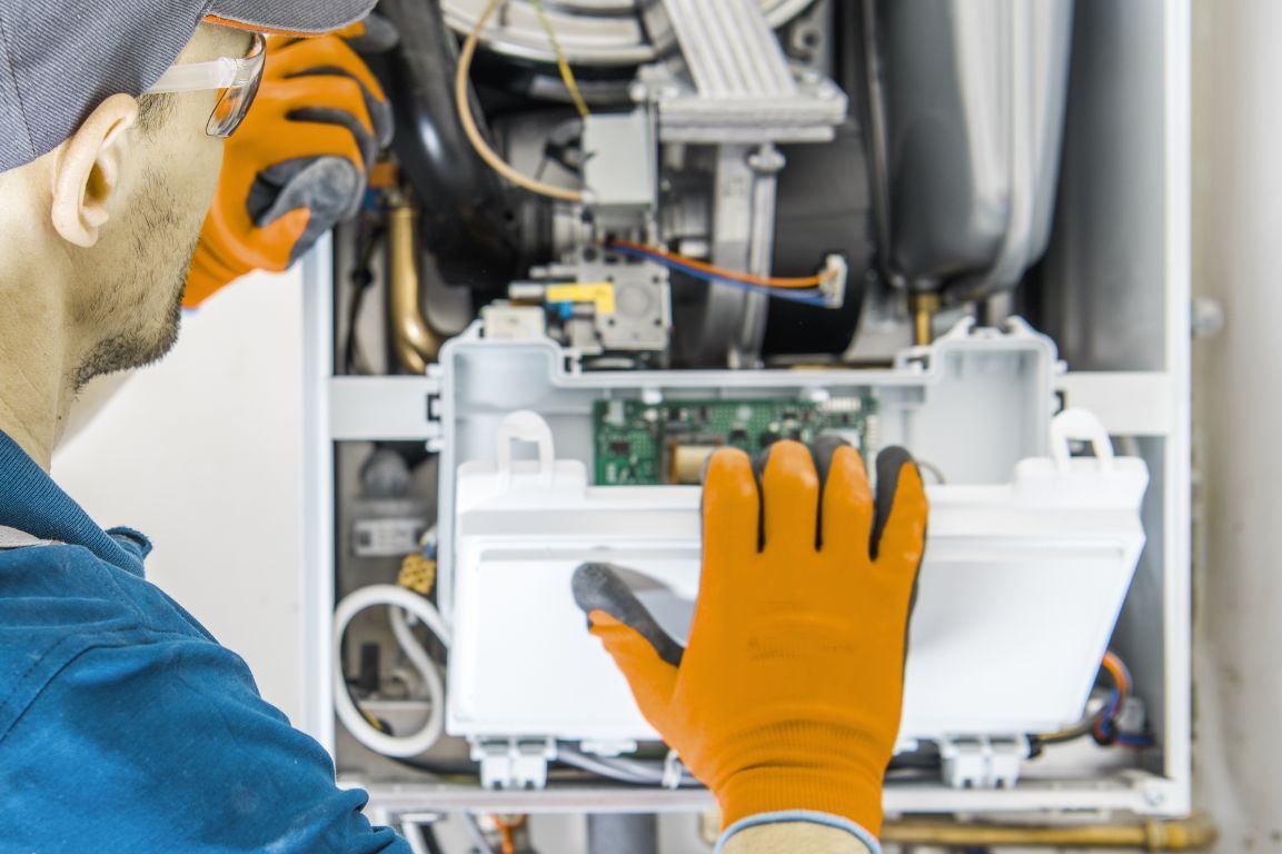 A man wearing orange gloves is working on a boiler.