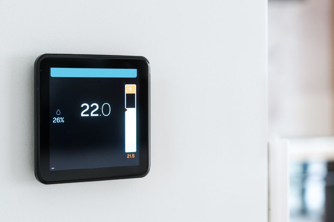 A smart thermostat is hanging on a white wall.