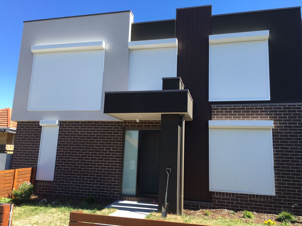 Outdoor patio with brown brick floor, retractable shades, and a backyard view.