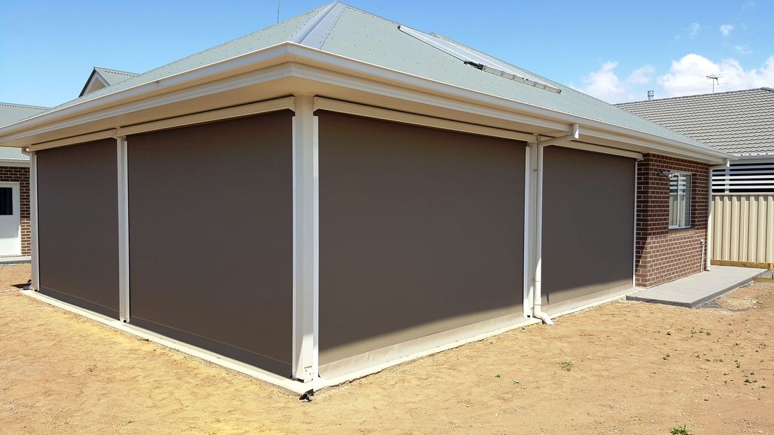Two gray outdoor blinds, on a brick house with a red roof, solar panels, and antenna.